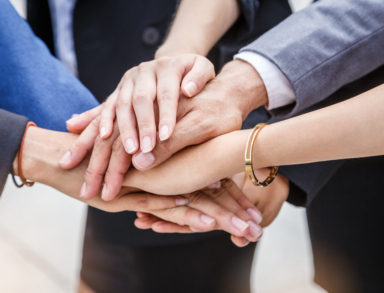 Mehrere Menschen legen ihre Hände übereinander als Zeichen von Teamarbeit und Zusammenhalt